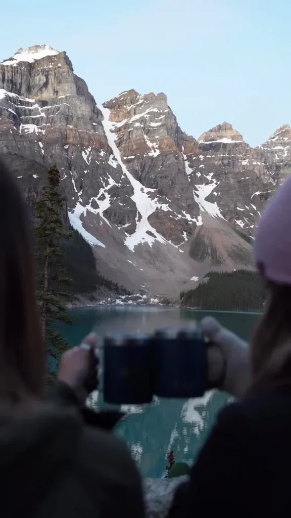 Two guests holding coffee mugs while looking toward Moraine Lake and the Valley of the Ten Peaks